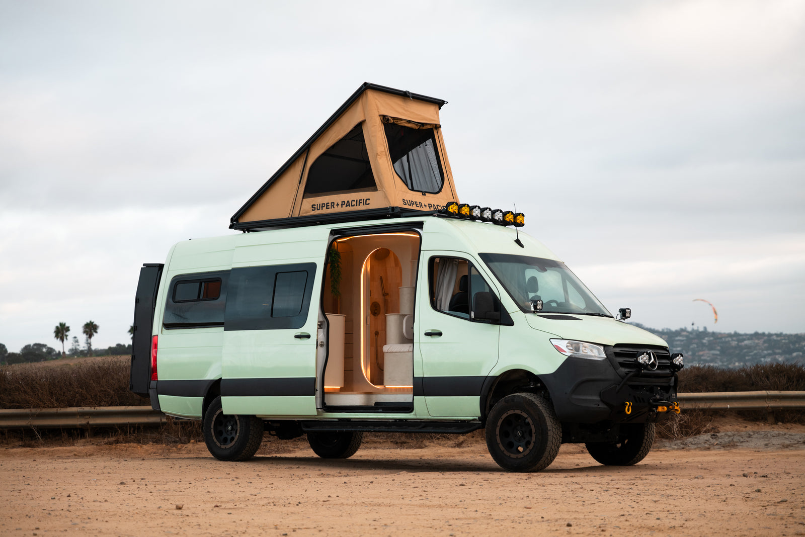 Flow parked near the coast with its side door and rooftop tent open