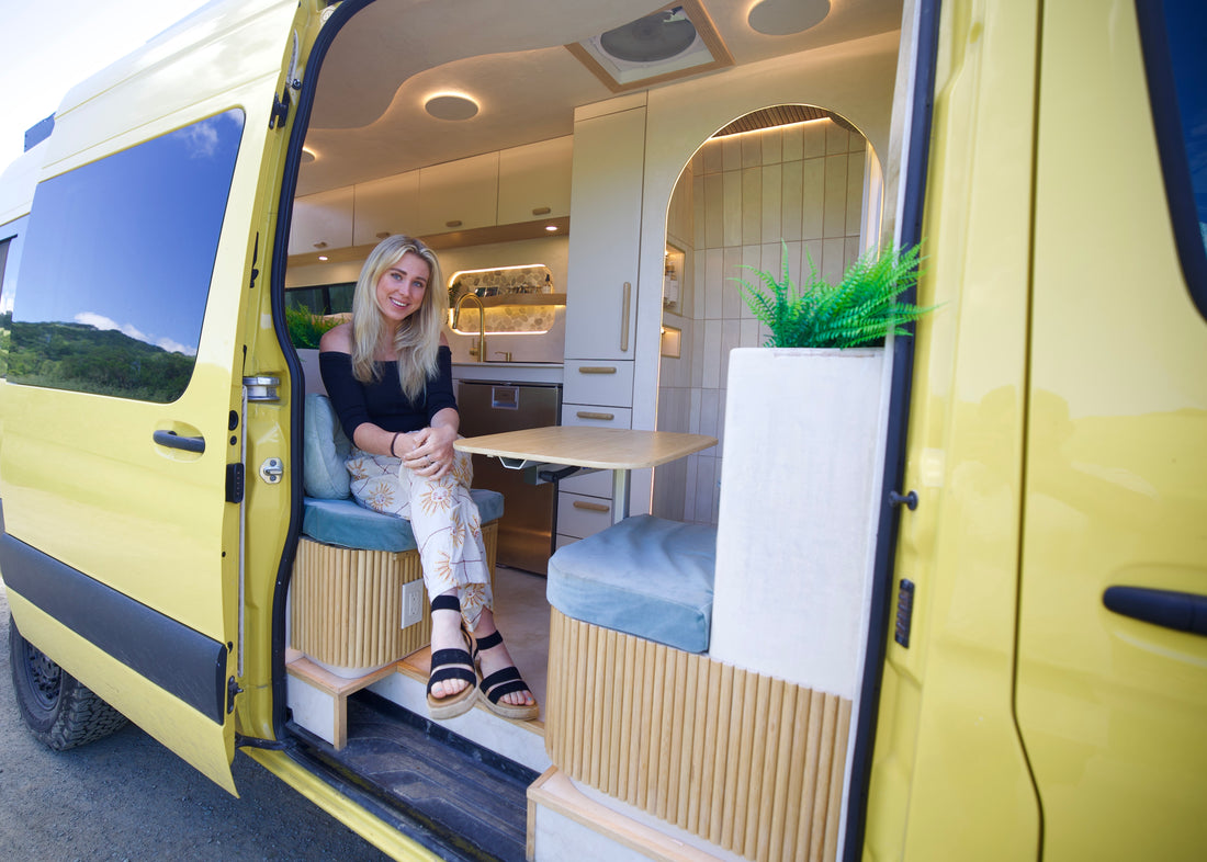 Abbe seated in the open doorway of the Luna, her yellow Sprinter conversion