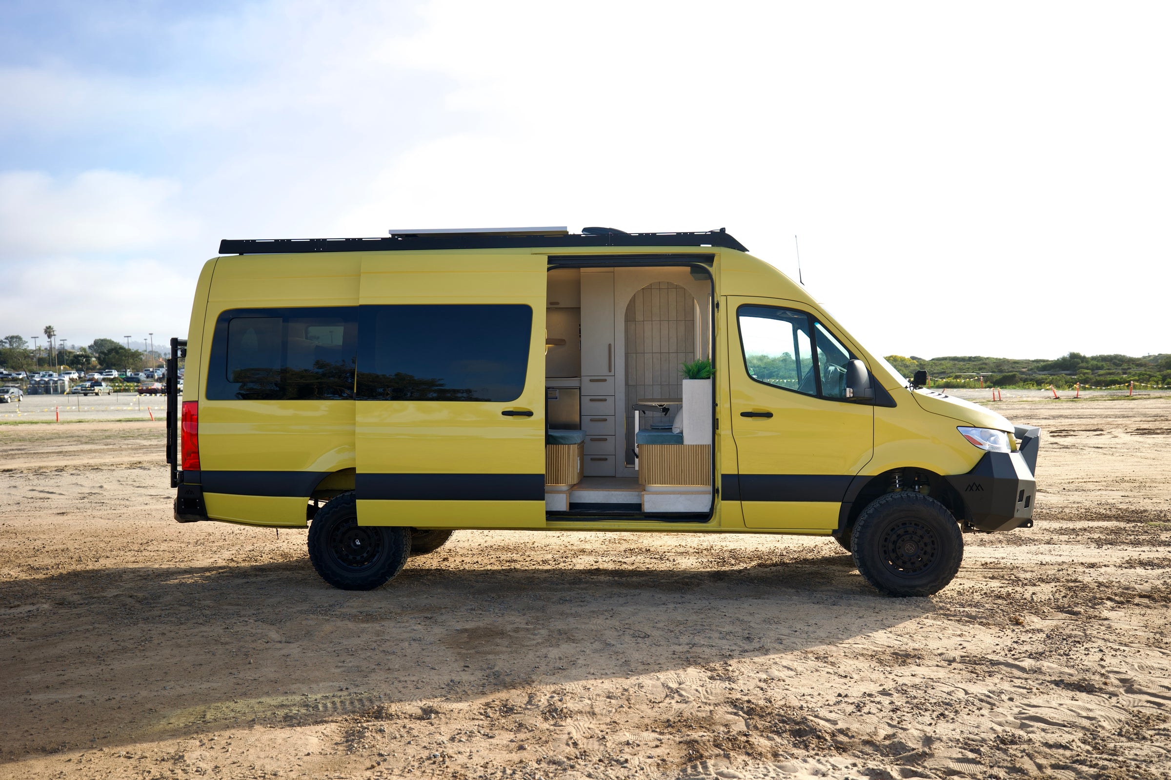 Side profile of the Luna, a yellow 4x4 Sprinter with roof rack and open slider door