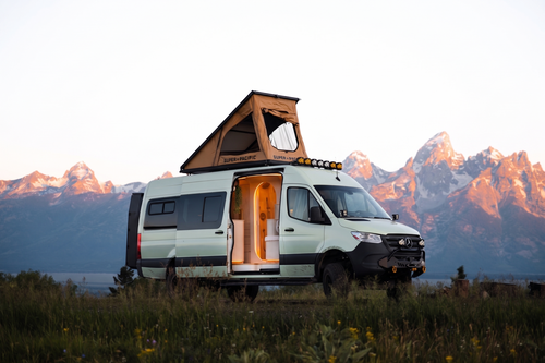 Flow parked in front of the Tetons at sunrise with the rooftop tent open and warm light inside