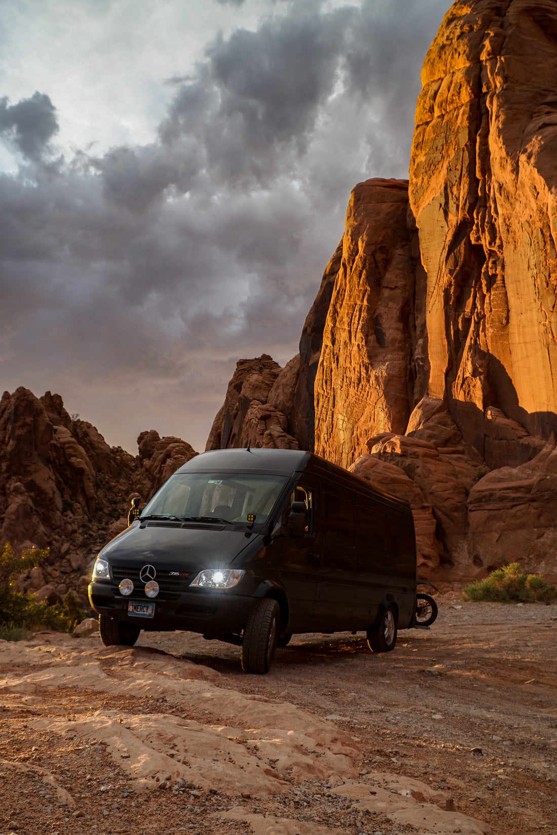 Abbe's first van, a black T1N Sprinter, parked beneath red rock cliffs at sunset