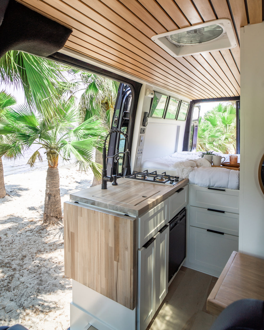 The Zen van's galley with wood slat ceiling, looking out to a palm-lined beach